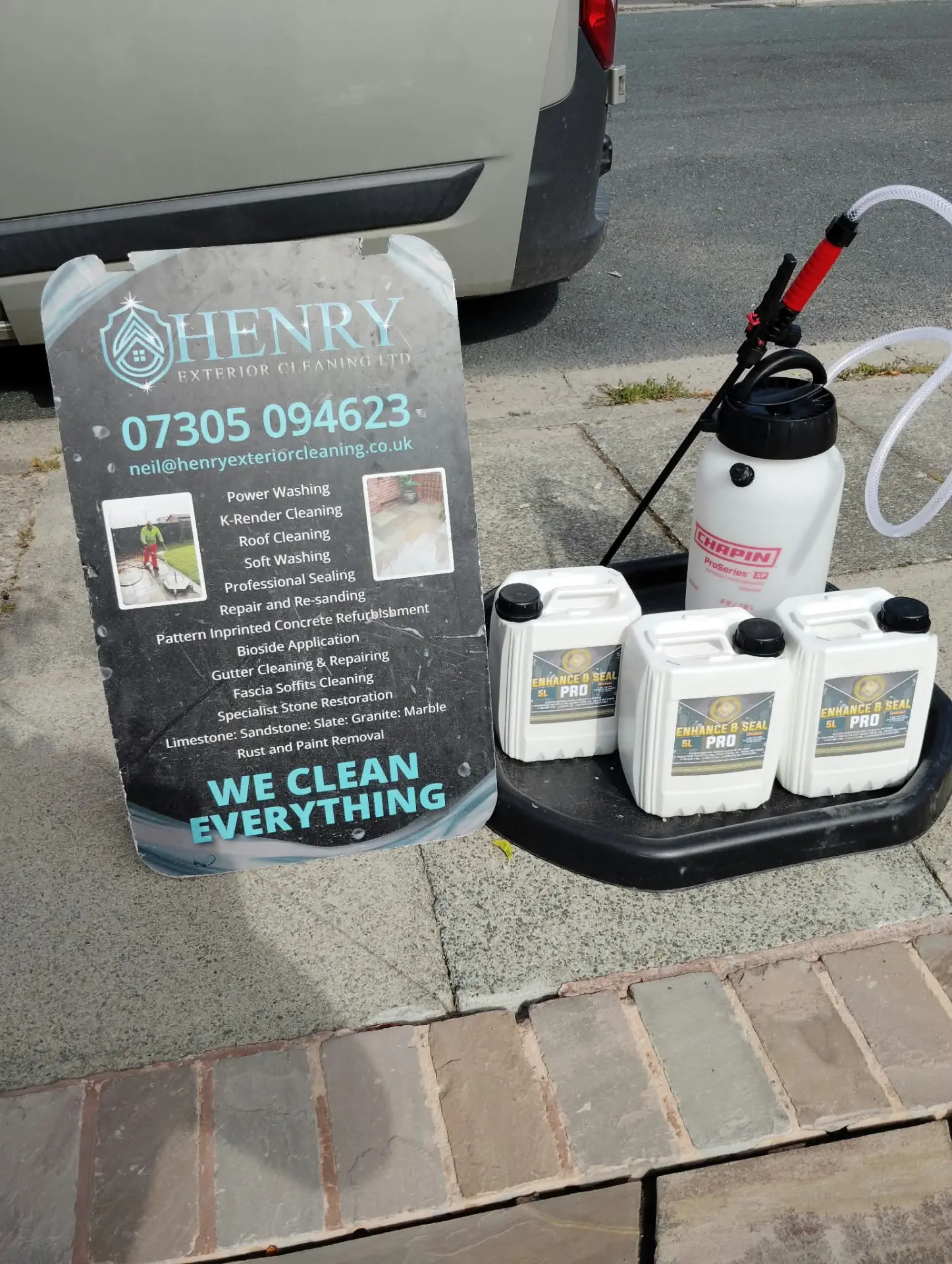 Henry Exterior Cleaning sign board with sealing products and sprayer on a sandstone path