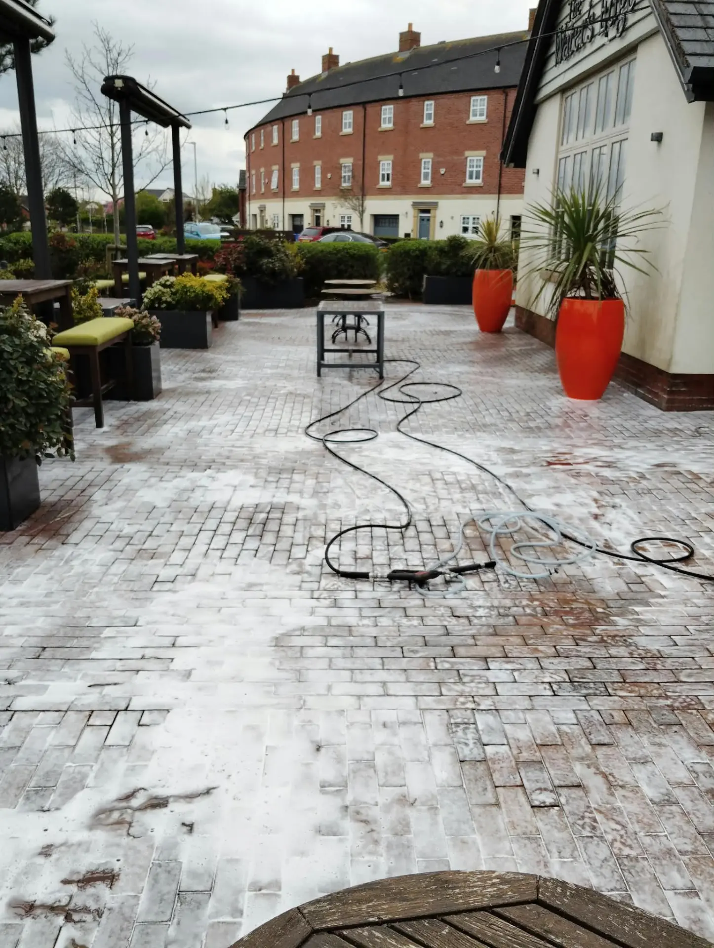 Outdoor dining terrace with clay block paving being pressure washed, hoses and equipment laid out