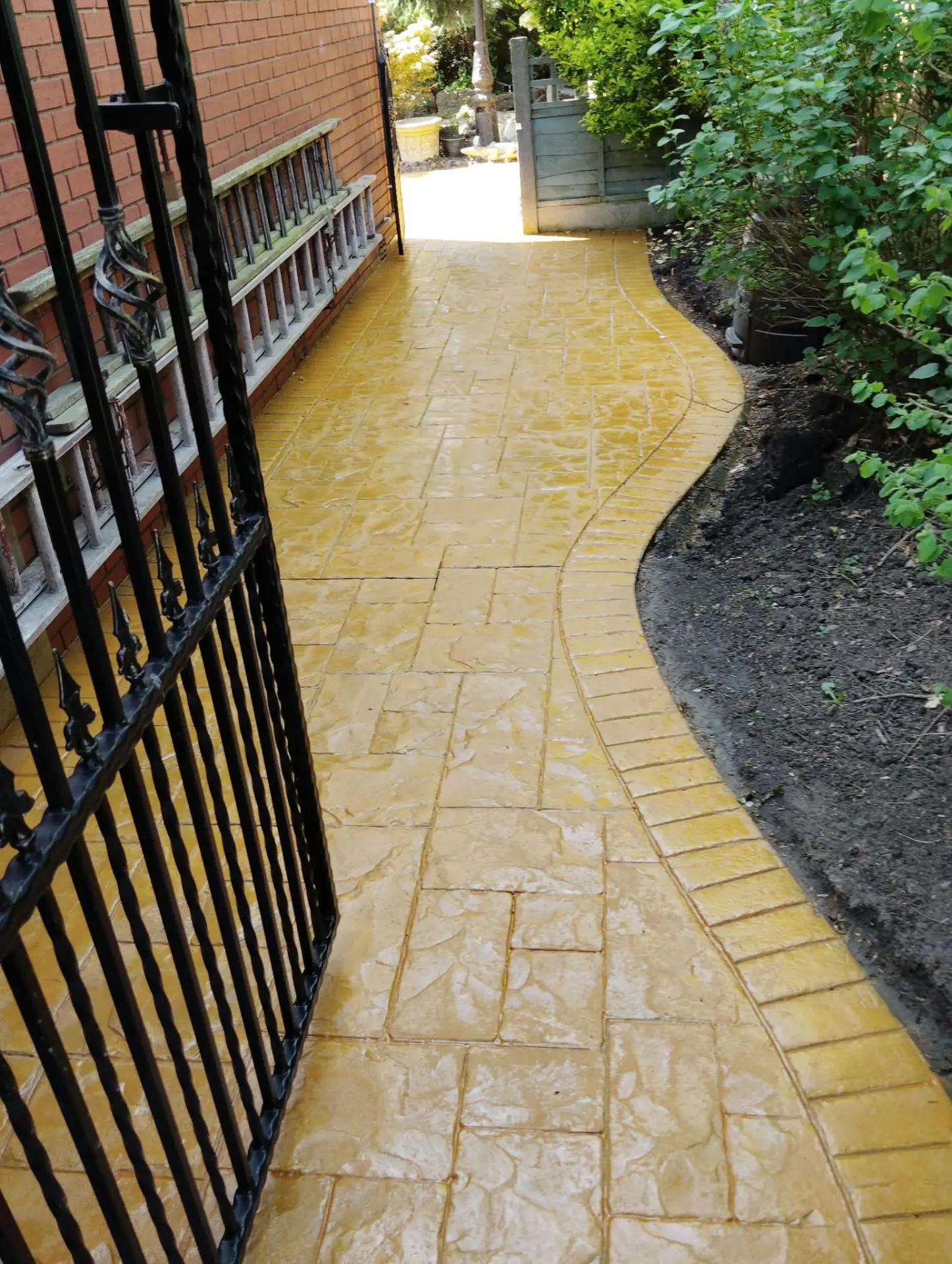 Sandstone coloured pattern imprinted concrete path resealed beside iron gates