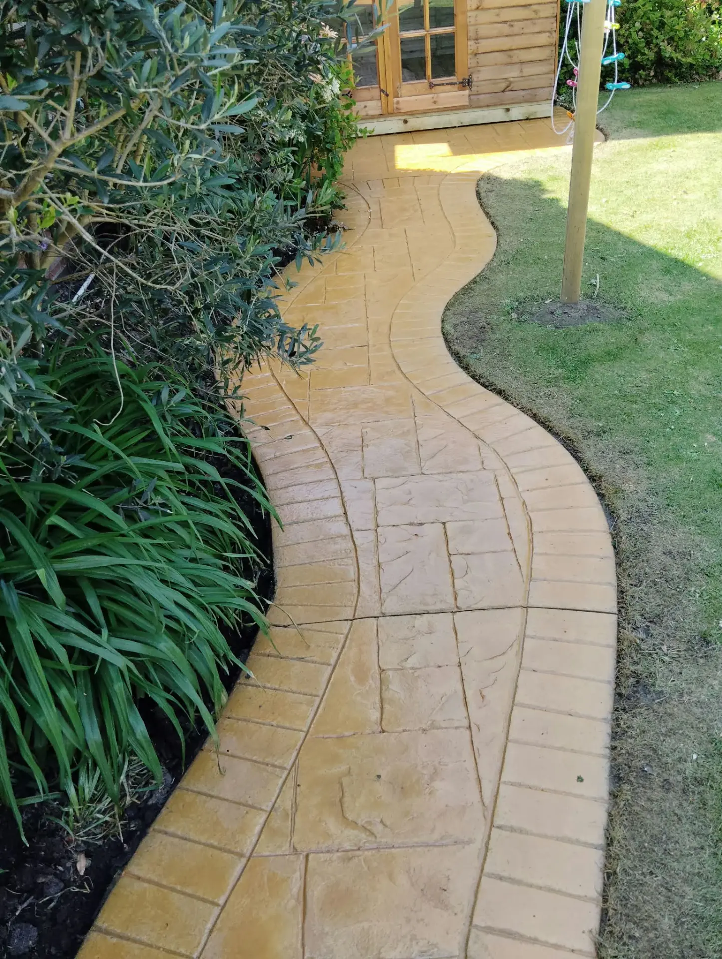 Curved buff pattern imprinted concrete path running past a garden border
