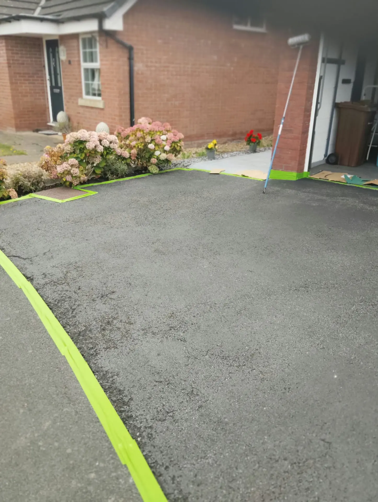 Faded grey tarmac driveway masked off with tape and cardboard before restoration