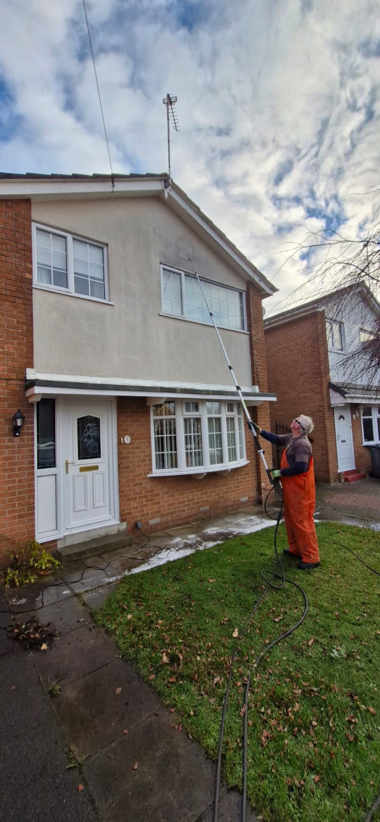 Operative soft washing the rendered front elevation of a semi-detached house