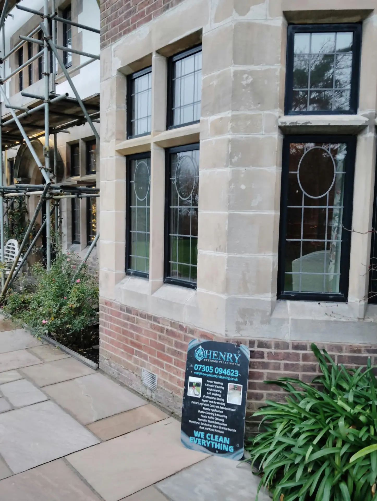 Restored sandstone mullioned bay windows with Henry Exterior Cleaning site board
