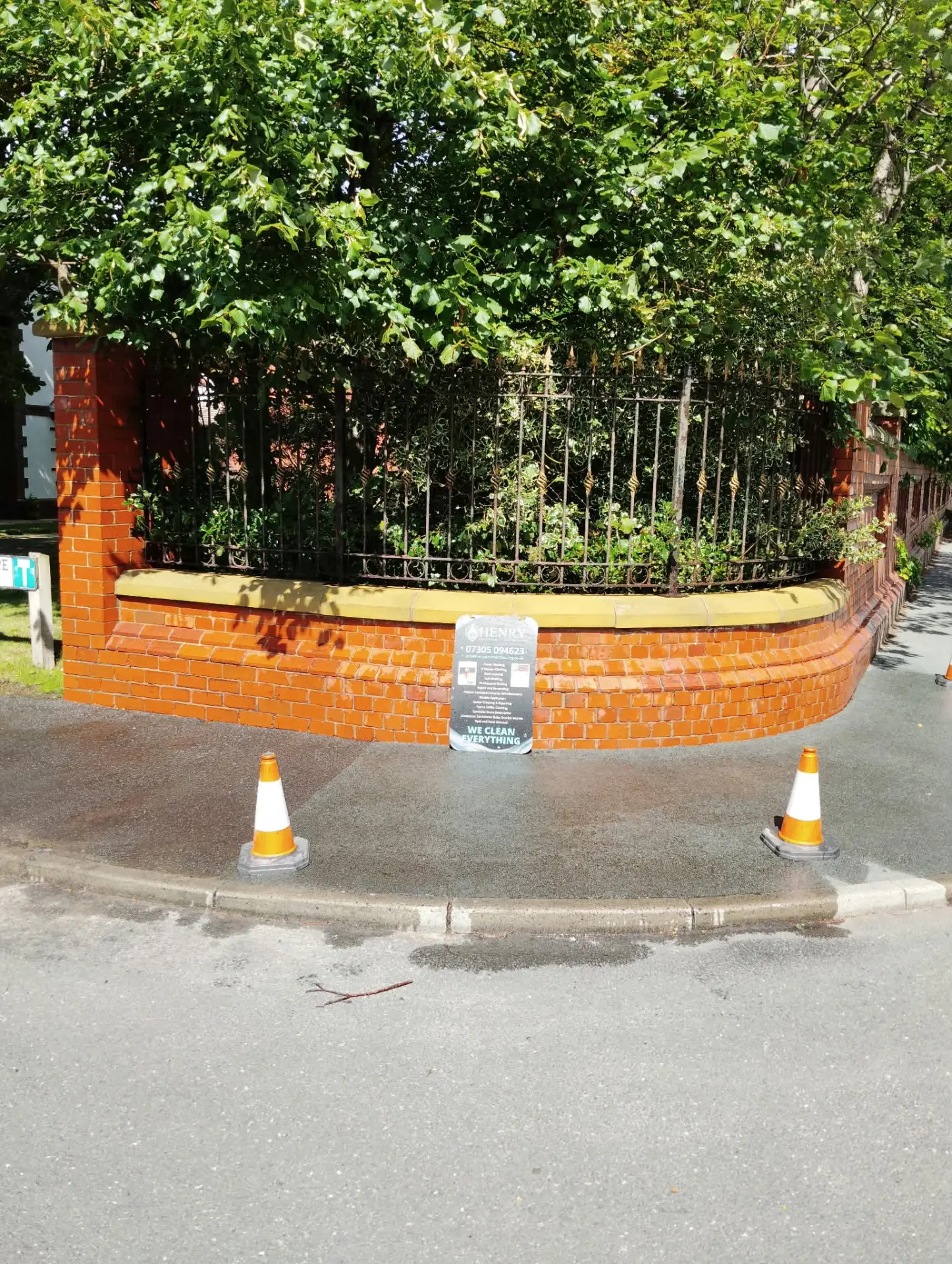 Curved red brick boundary wall acid cleaned back to a bright finish, coned off on the pavement