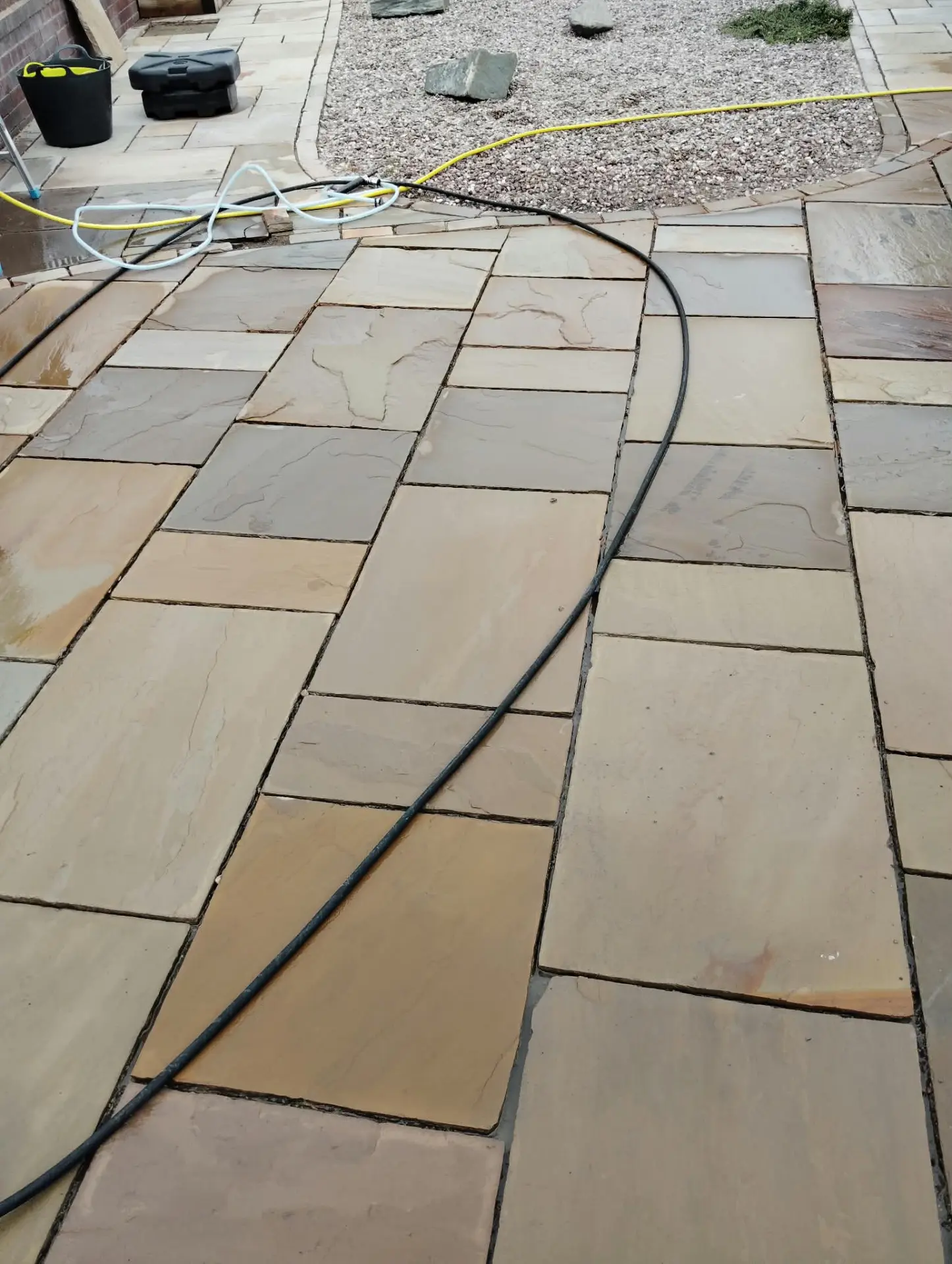 Indian sandstone patio mid-clean with hoses running across the wet flags