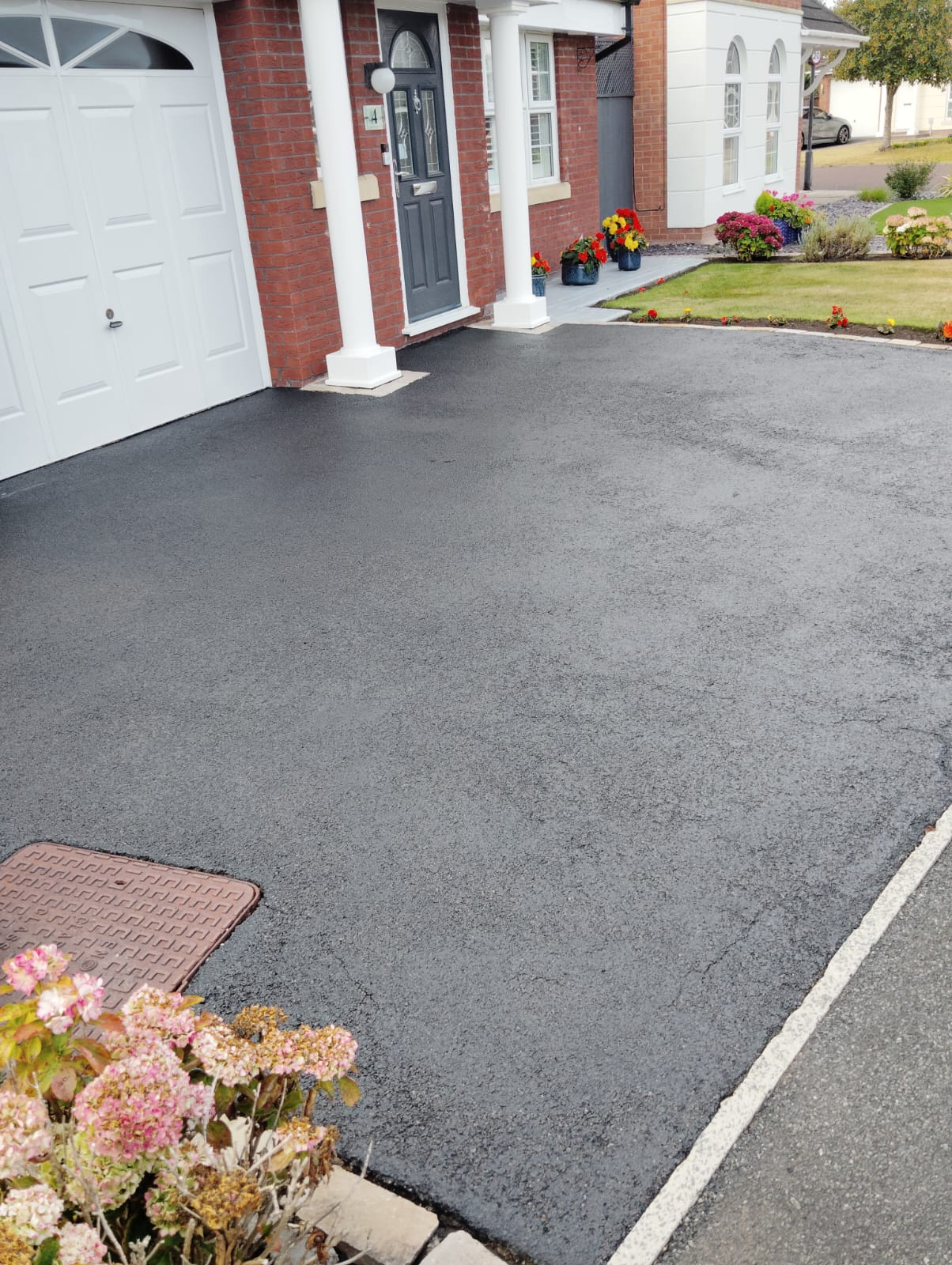 Completed tarmac driveway restoration in front of a red brick house
