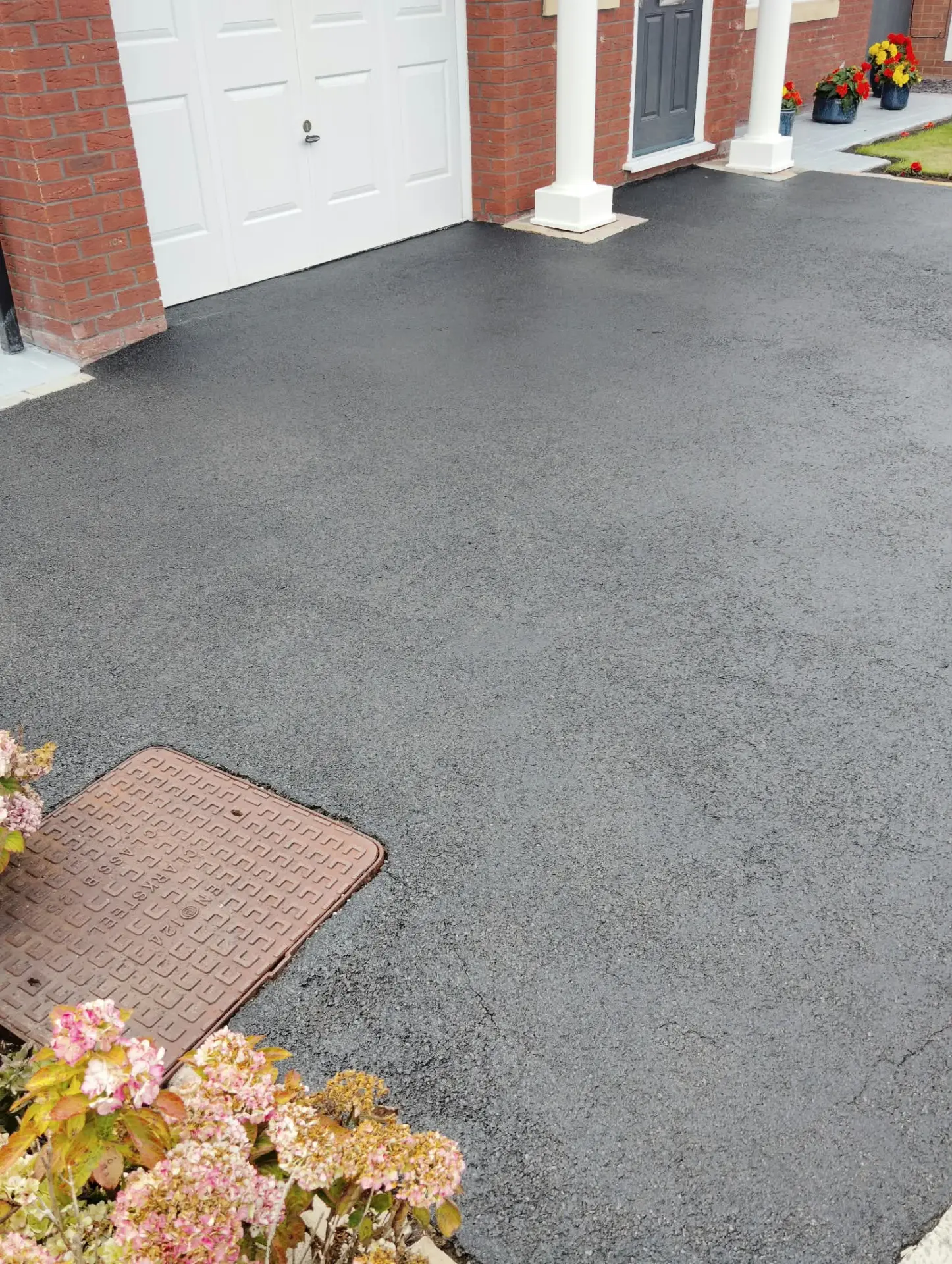 Freshly restored tarmac driveway with an even black finish around the garage and porch