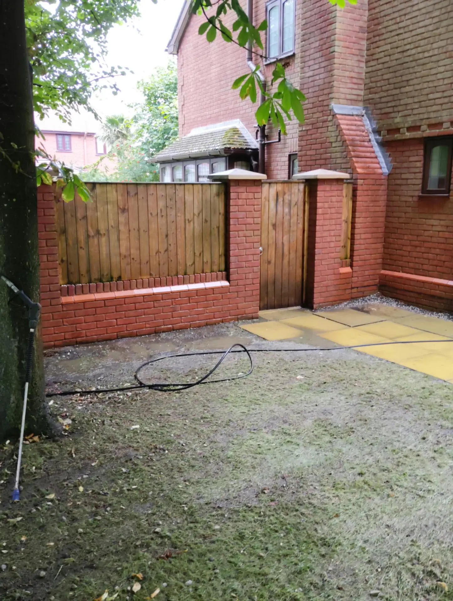 Brick wall and fence panels cleaned back to fresh colour beside a rear garden patio