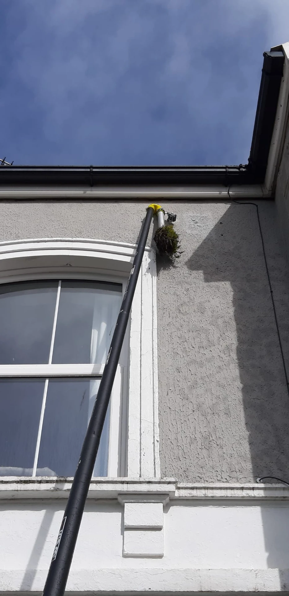 High-reach vacuum pole removing moss from gutter line on a rendered elevation