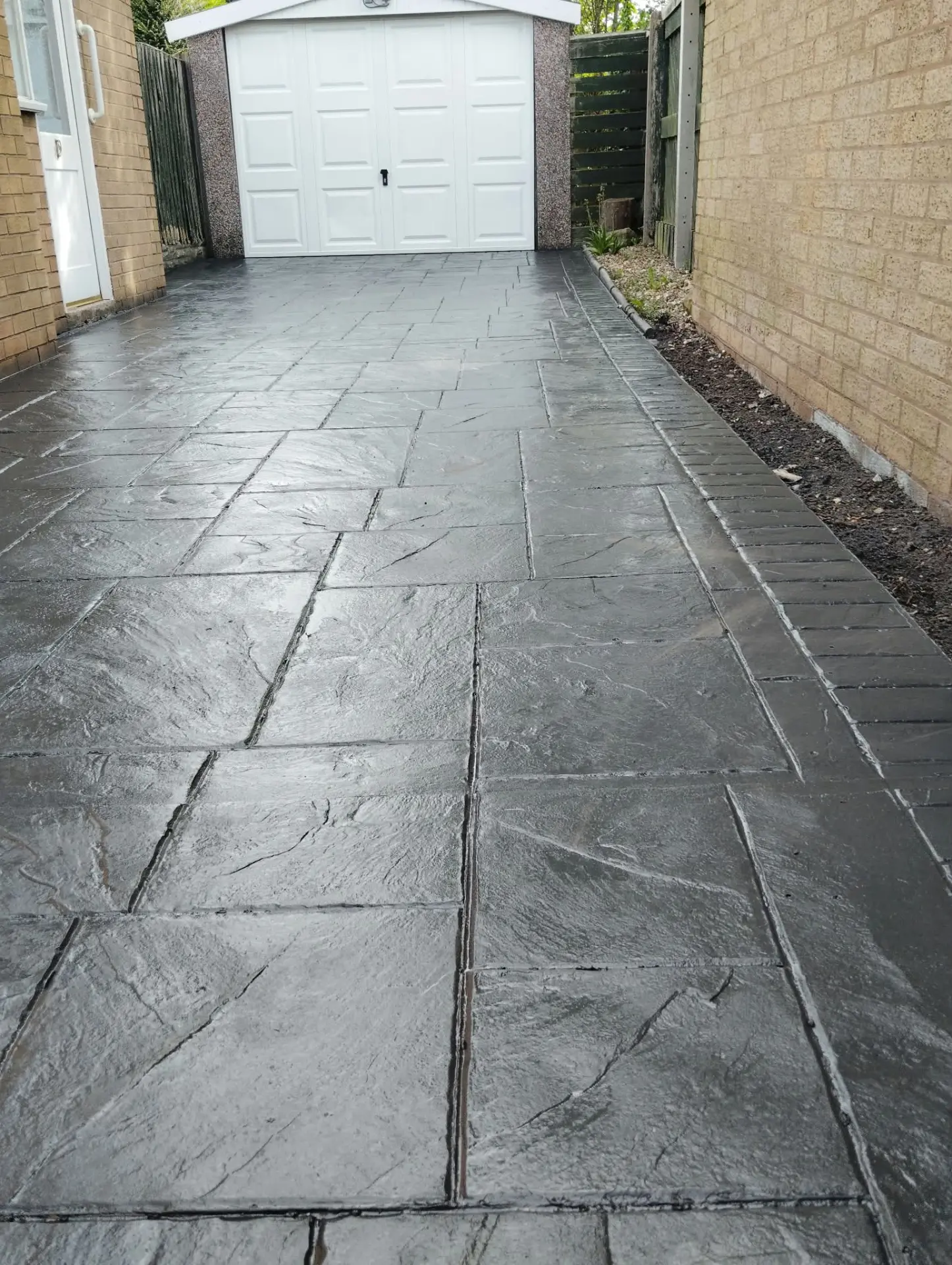 Slate grey pattern imprinted concrete driveway leading to a garage after sealing